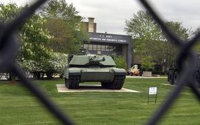 A view of a tank and the base sign on a building through the fence.
