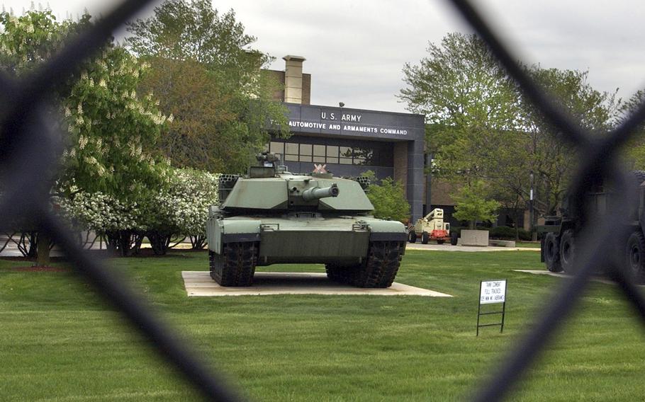 A view of a tank and the base sign on a building through the fence.