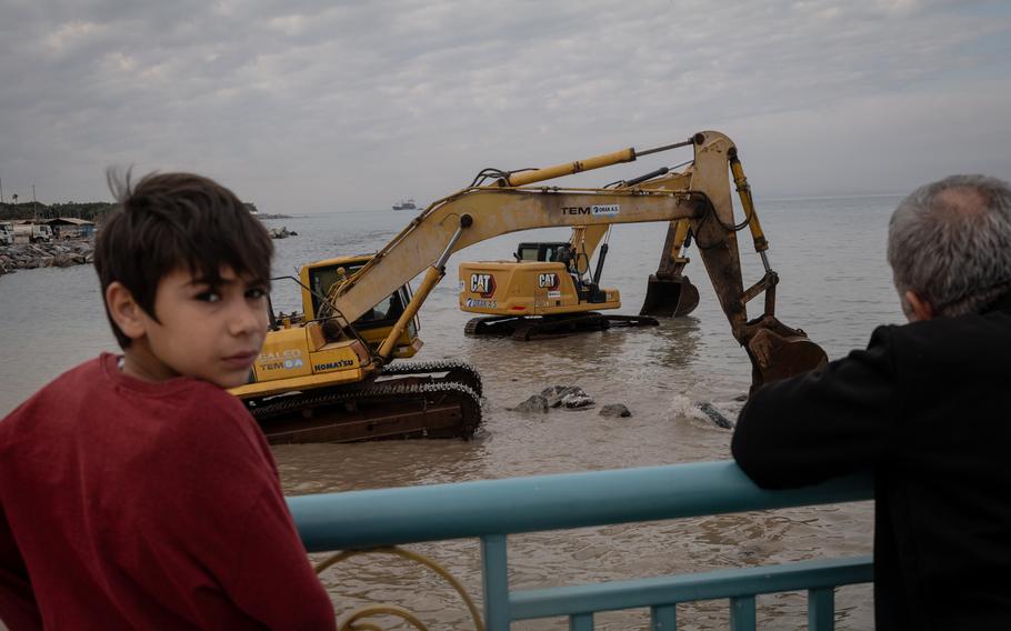 People watch as excavators work to rebuild waterfront barriers that were damaged in the quakes, causing regular flooding in the city of Iskenderun.
