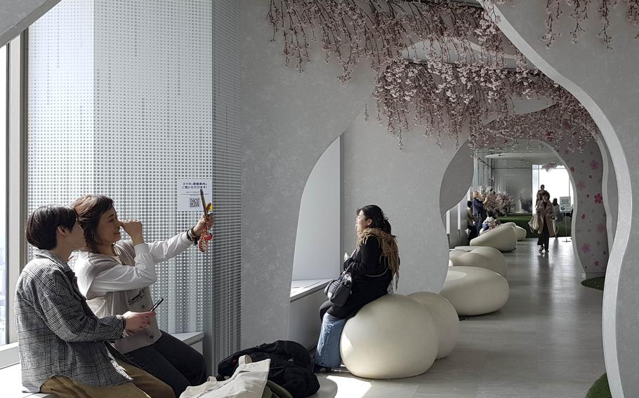 A couple takes a selfie in a hallway where pink blossoms decorate the pillars.