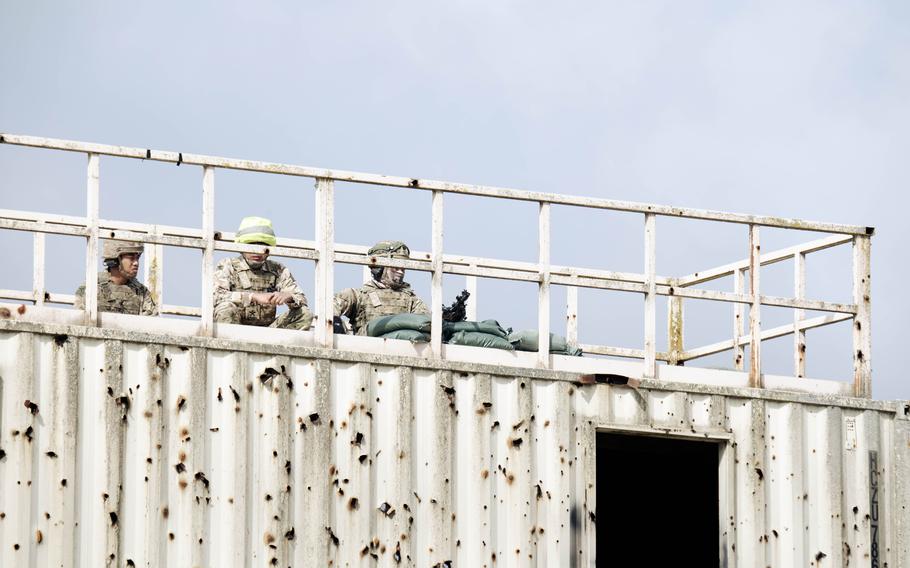 British soldiers position themselves on top of a rusted white watchtower to provide suppressive fire.