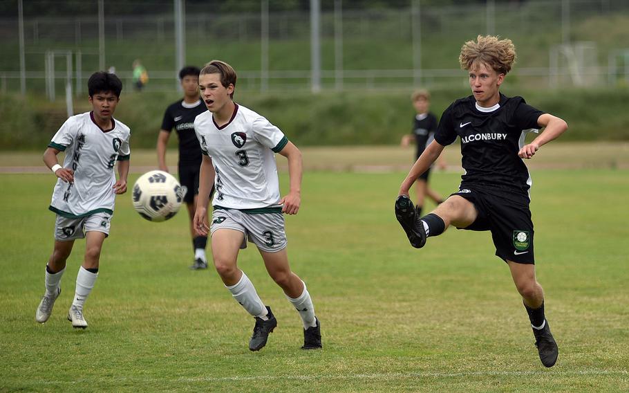 Alconbury striker Keiran Daley shoots the ball as Alconbury defenders Ben Maranon, left, and Sage Kallestad watch during a Division III semifinal match at the 2025 DODEA European championships on May 21, 2025, at Rothenborn Stadion in Landstuhl, Germany.