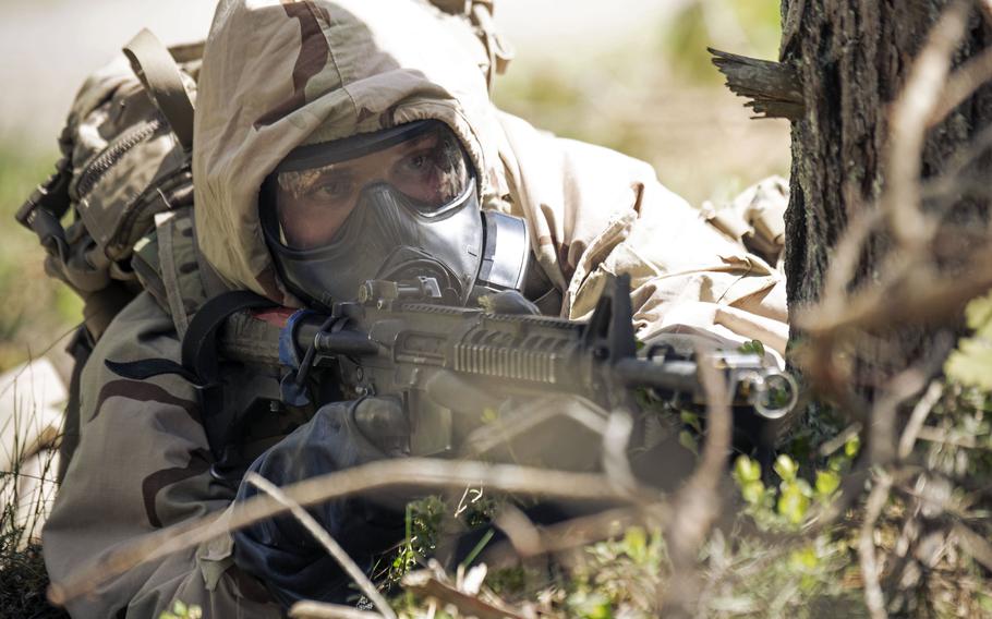 A soldier in a gas mask seen aiming a rifle while prone.