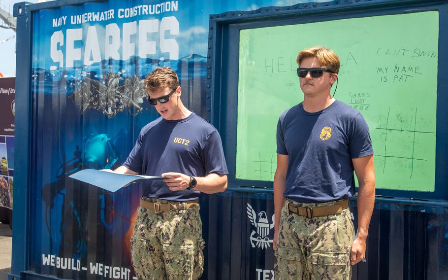 A sailor stands at attention while another sailor reads off a document
