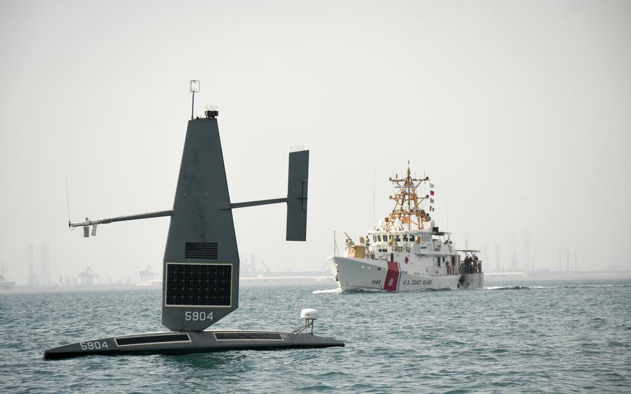 A Saildrone Explorer unmanned surface vessel passes in front of the crewed USCGC Emlen Tunnell, a Coast Guard cutter, on Nov. 30, 2022, in the waters of the Persian Gulf. The Navy has used drone boats in the Middle East for more than 25,000 hours over the last year, with the solar-powered Saildrone Explorers operating at sea for as long as 220 consecutive days.