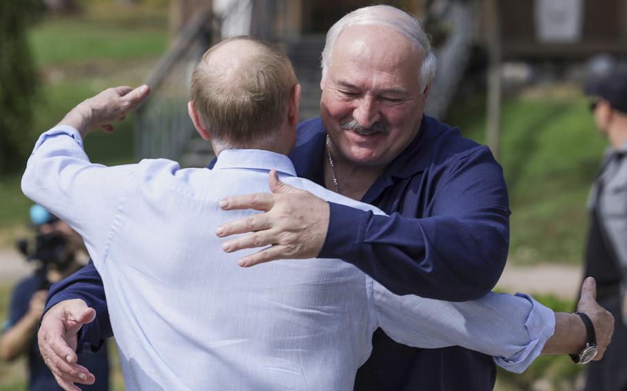 The back of Vladimir Putin seen embracing the leader of Belarus, who can be seen smiling.