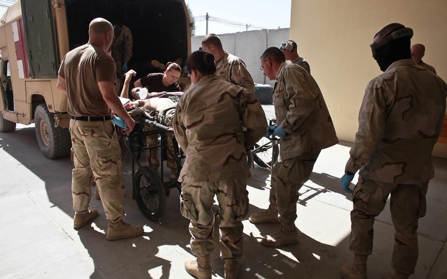 Soldiers wheel an injured person onto the back of a military vehicle