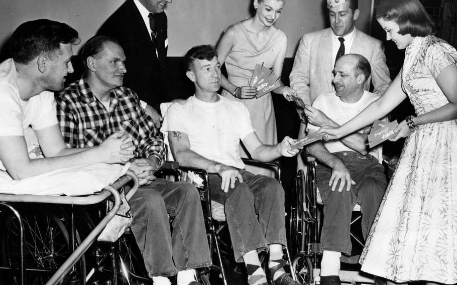 Harold G. LeRoy, the Cook County commander of Amvets, standing from left, model Carol Butler, Tim Cornell, senior vice-commander of Amvets, and Rusti Salmon hand out presents to 250 veterans at Hines Hospital on Dec. 9, 1955. The veterans are, from left, Boyd Bergheffer, 34, Chester, 50, Robert McKain, 40, and Erwin Steinberg, 40.