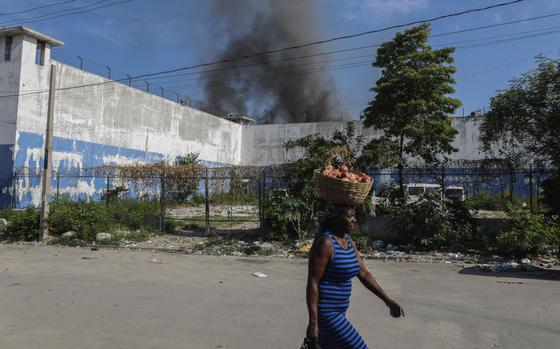 A woman walks past the smoking, empty National Penitentiary after a small fire broke out inside the jail in downtown Port-au-Prince, Haiti, Haiti, Thursday, March 14, 2024. This is the same prison that armed gangs stormed late March 2 and hundreds of inmates escaped. (AP Photo/Odelyn Joseph)