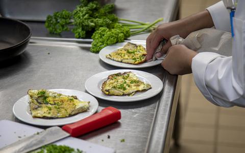 A pair of hands uses a towel to wipe one of three plates of food on a stainless steel countertop.