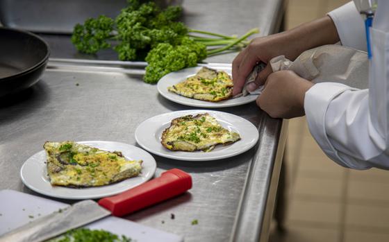 A pair of hands uses a towel to wipe one of three plates of food on a stainless steel countertop.