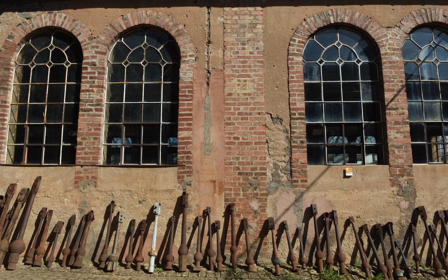A row of old bell clappers is propped up along a wall in the courtyard of the Museum of Bell Foundry Mabilon in Saarburg, Germany. Some of the clappers show dents from years of use. The museum showcases a workshop that cast bronze bells for more than 230 years before it closed in 2002.