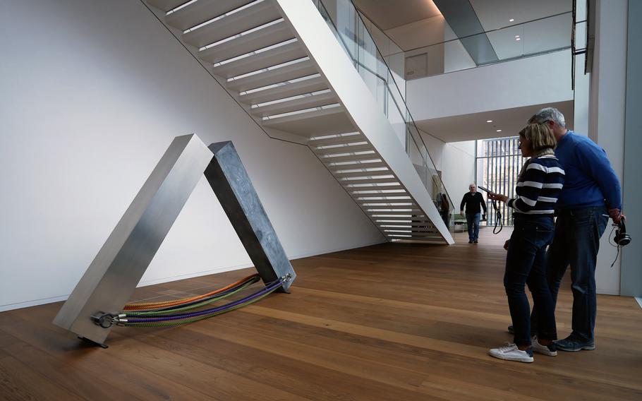 A sculpture by an artist stands under a staircase at an art museum