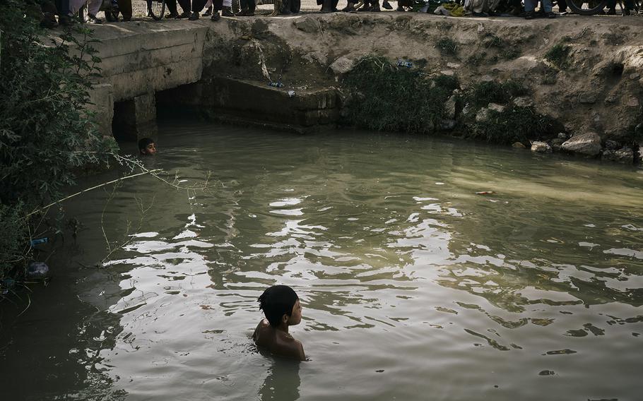 Children swim in a canal near the destroyed bazaar in Marja, on June 13, 2022.