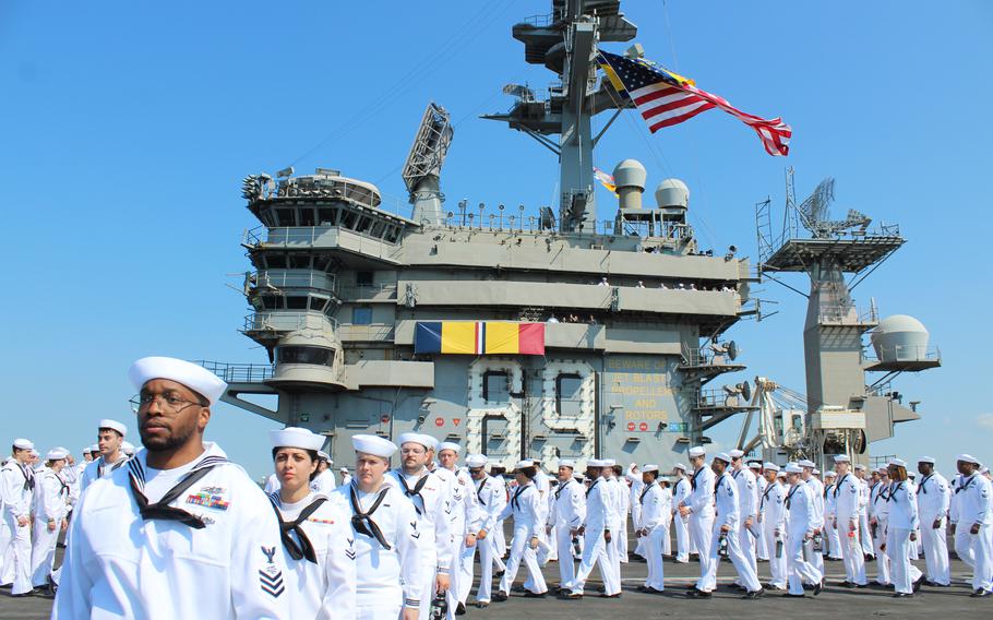 Sailors aboard the USS Dwight D. Eisenhower begin to man the rails on Sunday, July 14, 2024, as the aircraft carrier approaches Naval Station Norfolk, Va. A banner replica of the combat action ribbon was strung across the island of the ship. The Eisenhower returned to Norfolk from a twice-extended deployment to the Red Sea where it defended other ships against almost daily attacks from Houthi rebels in Yemen.
