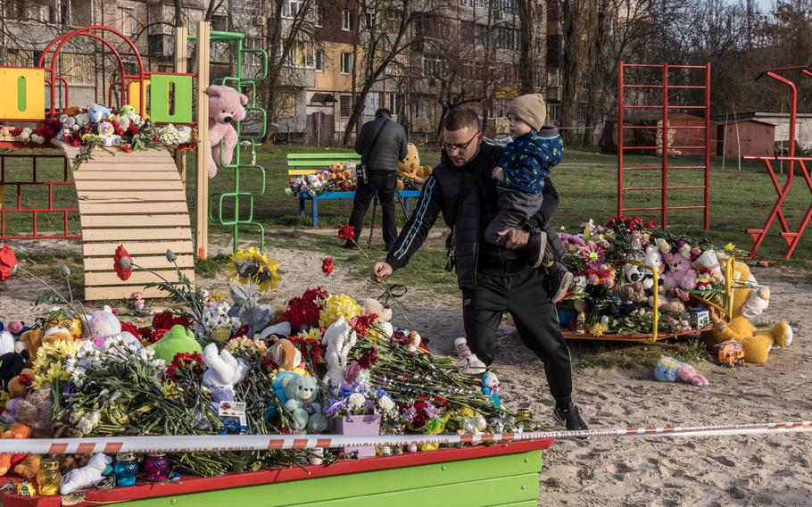 A man holds a child and places flowers at a playground.