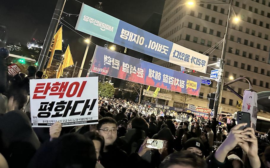A crowd of demonstrators with signs and banners gathers at night at the National Assembly in Seoul.