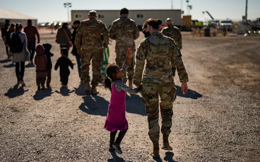 A U.S. military service member holds the hand of an Afghan refugee girl as they walk inside a camp at Holloman Air Force Base in Alamogordo, N.M., on Nov. 4, 2021. 