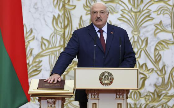 Alexander Lukashenko stands at a podium while placing one hand on a book on another podium next to him.