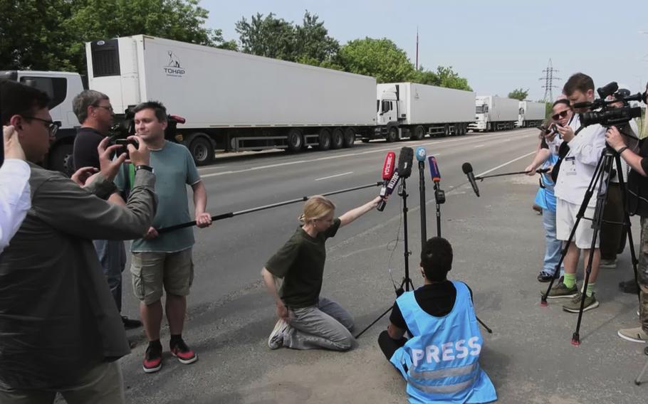 Reporters with microphones and cameras. Refrigerated trucks are in the background.
