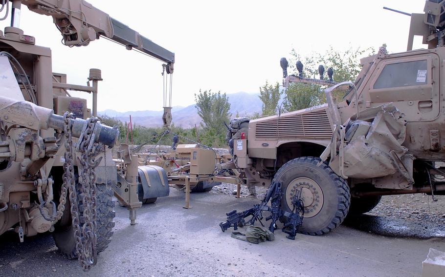 Two military vehicles, one with a crane attached, in a mountainous setting.