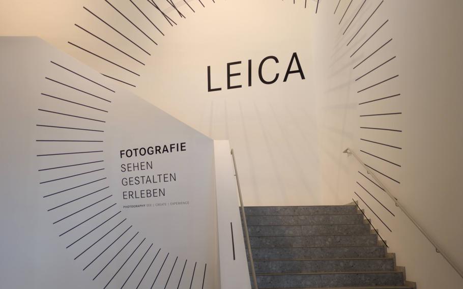 Painting on a white wall around a stairway reads “Leica Fotographie Sehen Gestalten Erleben” in German.