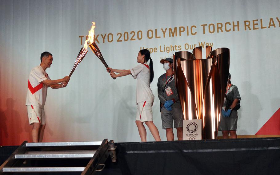 Torch relay runners from Hamura, a city near Yokota Air Base, pass the Olympic flame during an indoor ceremony in Tachikawa, Japan, Monday, July 12, 2021.