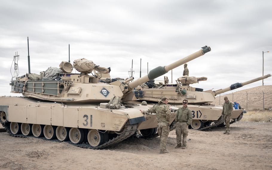 Soldiers stand in front of two tanks.
