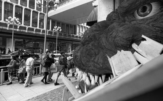 Shibuya, Tokyo, Japan, December 11, 1991: Children and adults alike do a double take as they see Godzilla burst through onto the streets of Tokyo. Part of a promotion for the newest Godzilla movie "Godzilla vs. King Ghidorah," the head of the giant, nuclear empowered prehistoric sea monster, crashes through a wooden box in front of the Seibu department store in the Shibuya neighborhood of Tokyo. Did you know that a Godzilla slide exists in Yokosuka? Read about it on Stripes' Okinawa Community site https://okinawa.stripes.com/travel/seaside-city-where-godzilla-found-home META TAGS: Pacific; entertainment; Tokusatsu; kaiju; film; movie; advertisement; film promotion; Japanese culture; science fiction; sci-fi;