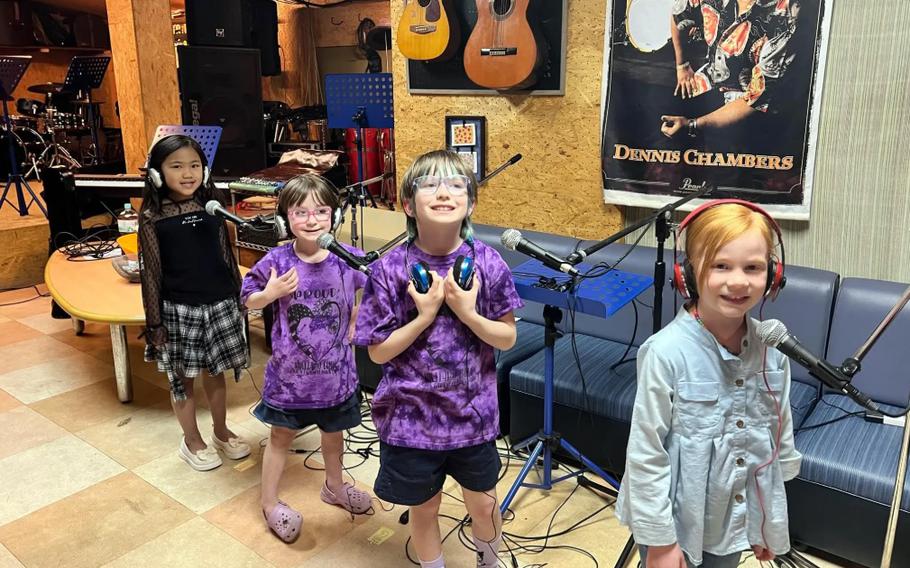 Children wearing headphones pose in front of microphones.