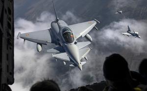 Light gray fighter jets are seen from above as they fly over a landscape.