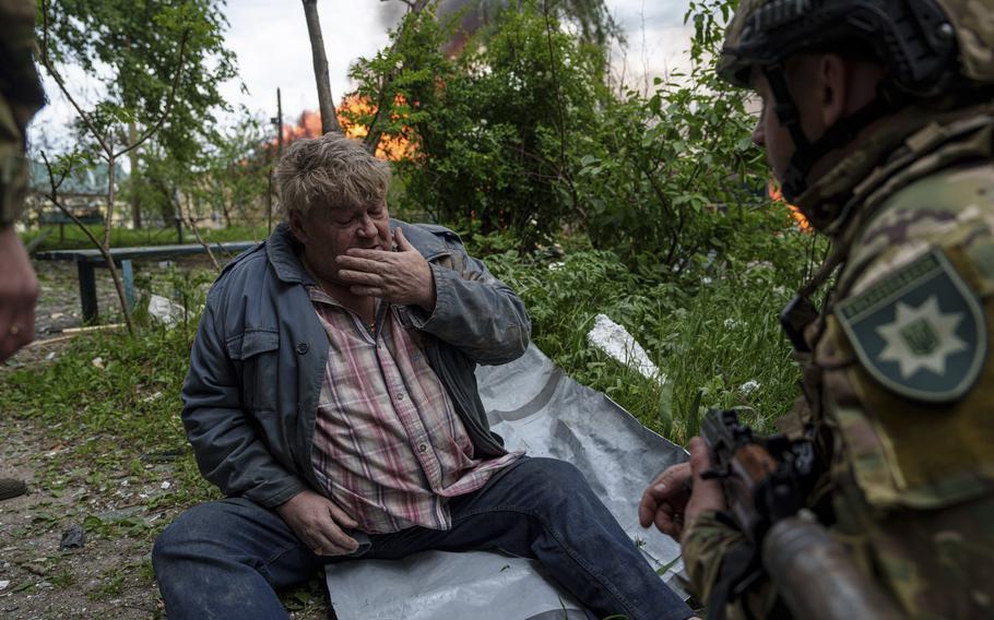 A police officer speaks to a local man as his house is seen on fire after a Russian airstrike in Vovchansk, Ukraine, on Saturday, May 11, 2024. 