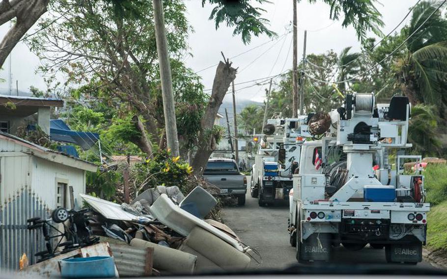 Two utility maintenance trucks navigate a narrow street cluttered with debris near San Juan, Puerto Rico, on Nov. 10, 2017, as National Guard members try to restore electrical power months after Hurricane Maria devastated the island.