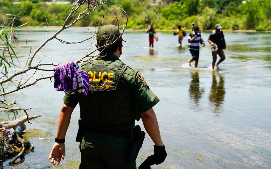 A Border Patrol agent watches as a group of migrants walk across the Rio Grande on their way to turn themselves in upon crossing the U.S.-Mexico border in Del Rio, Texas.