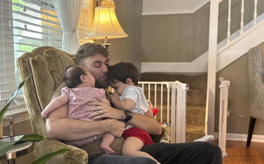 A man holds his young children while sitting in a chair.