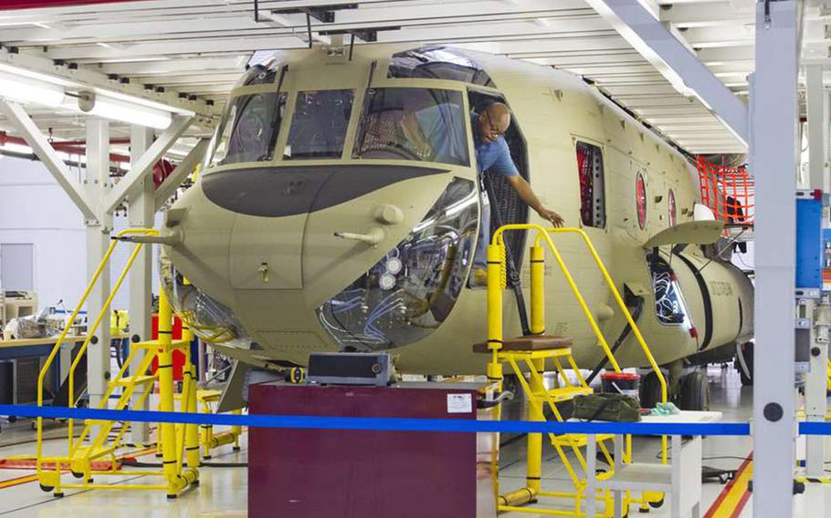 A man climbs out of the cockpit of a helicopter onto a ladder as it sits in a factory while under construction.