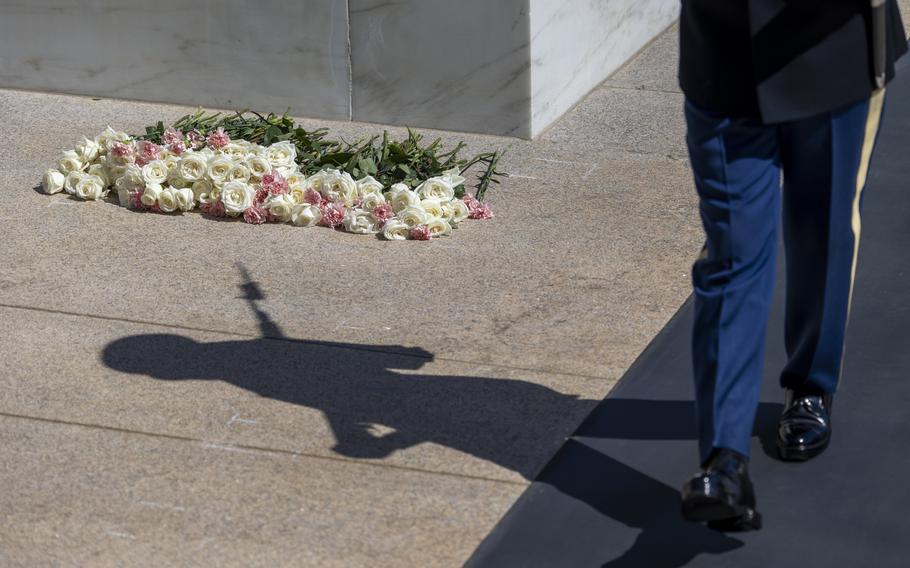 A soldier marches past flowers on the ground next to the tomb.