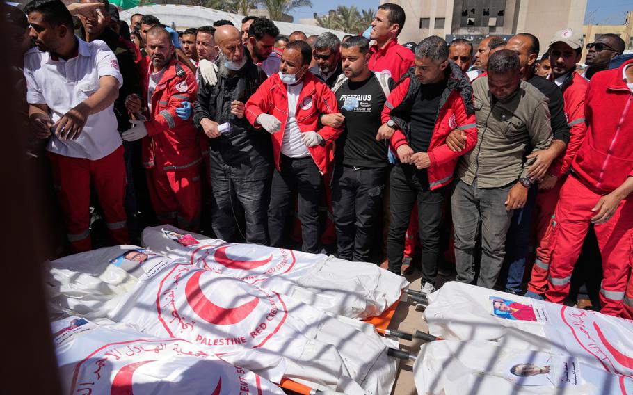 People lock arms as they gather around the covered bodies of emergency responders.