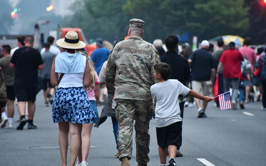 A military family walks amongst a crowd, with a young boy waving an American flag.