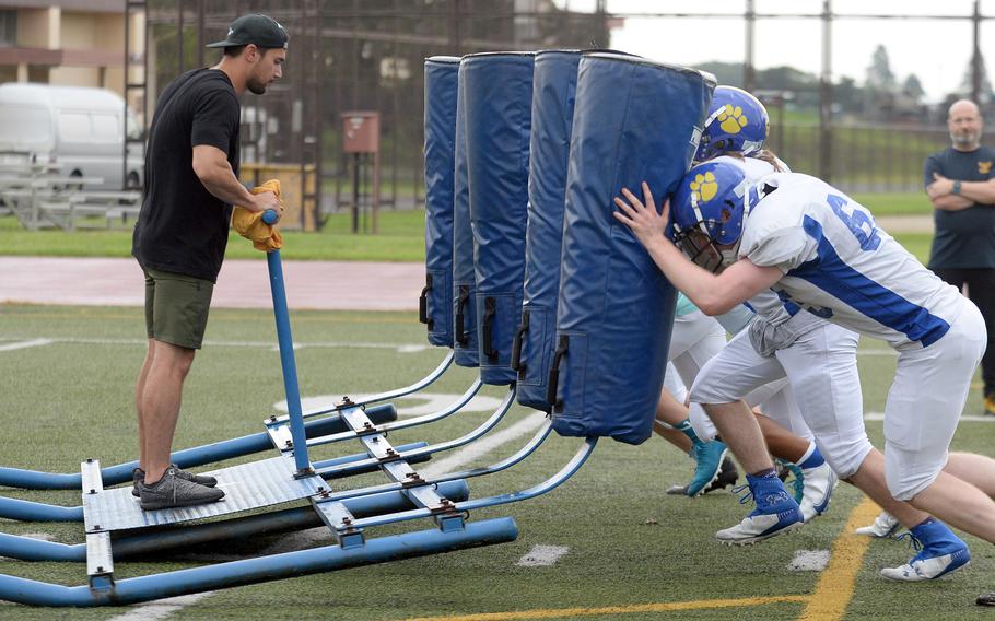 Yokota assistant coach Aaron Gove gets a ride on the blocking sled from Yokota's offensive line; co-head coach Michael Woodworth watches in the background.