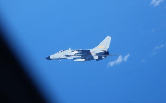 A military fighter aircraft flies against a bright blue sky with scattered white clouds.