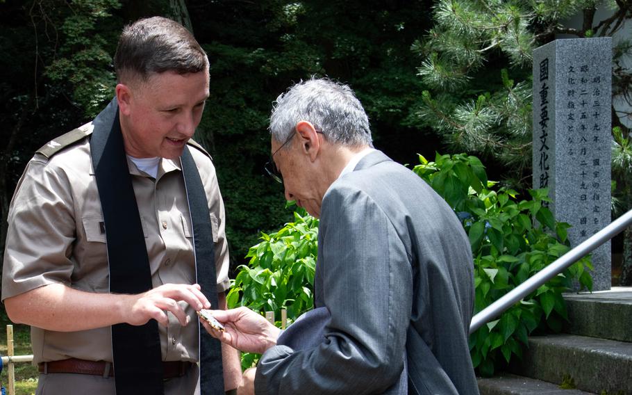 A U.S. Army chaplain hands a coin to a Japanese man.