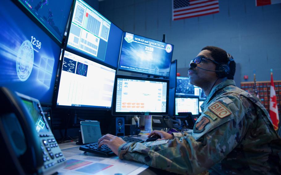 An airman in front of computer monitors.