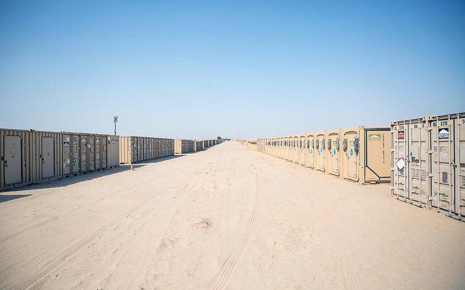 An avenue of sand lined with beige storage containers on either side, stretching into the distance.