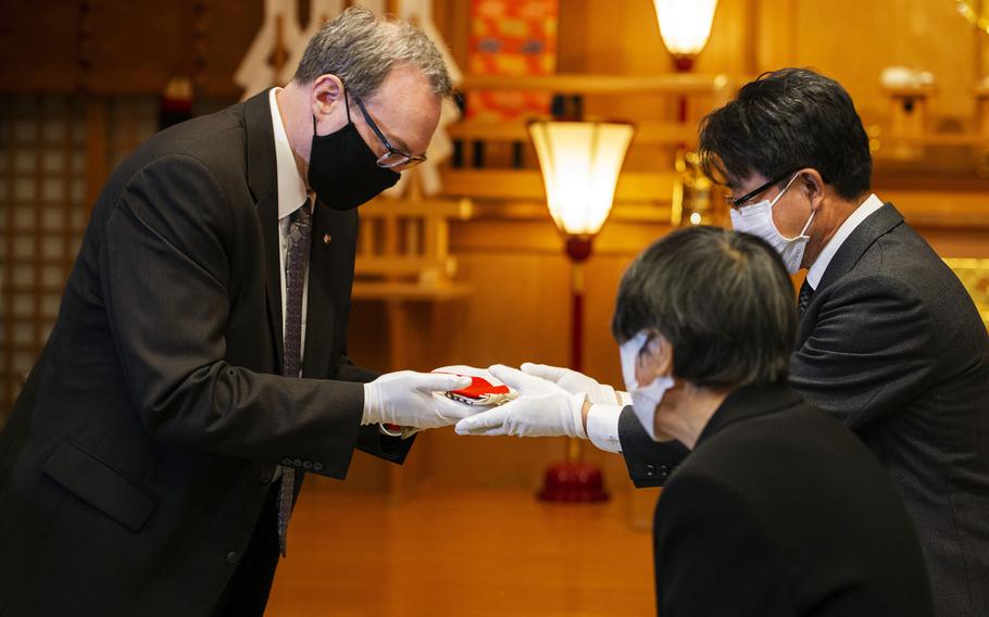 Chris Johnson returns Norito Myochin's "good luck flag" to the late Japanese sailor's relatives, nephew Toshinari Myochin and sister Keiko Hirota, during a ceremony at Gokoku Shrine in Hiroshima, Japan, Sunday, Dec. 4, 2022.