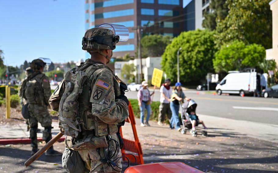 National Guard members stand outside of a federal building and watch a family walk buy pushing a stroller.