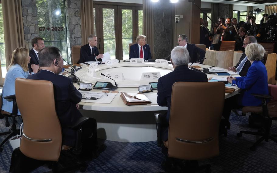 Donald Trump and other world leaders sit at a round conference table with glasses double doors behind them.