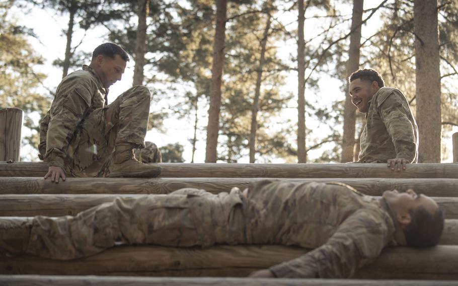 Three soldiers in a forest, two sitting and one lying down.
