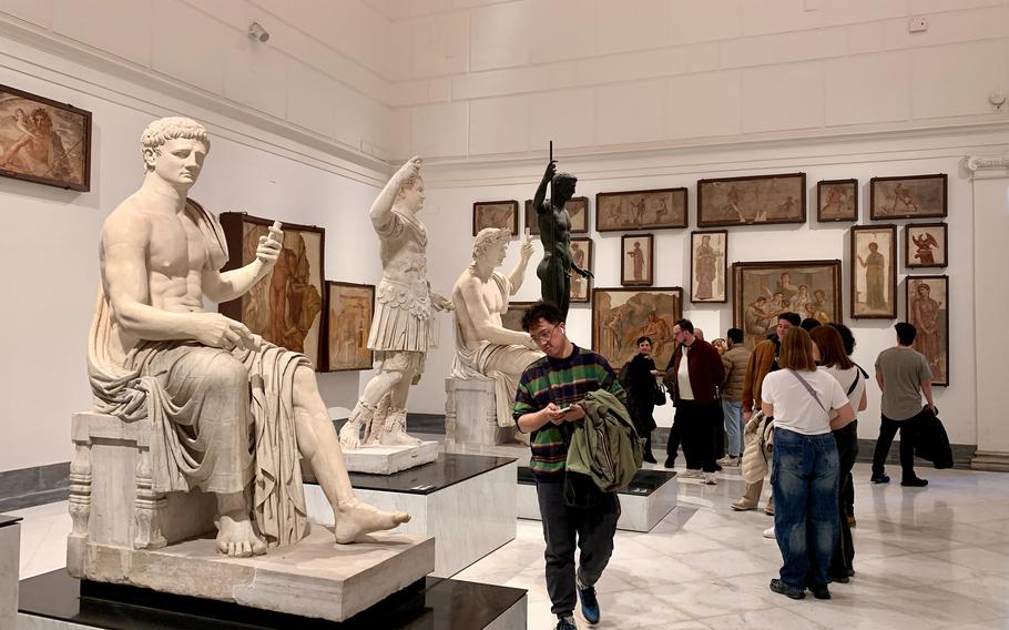 A couple of marble statues with visitors looking at them in a room.
