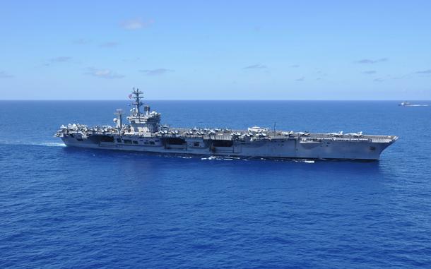 An aircraft carrier sails in open ocean with the horizon in the background.